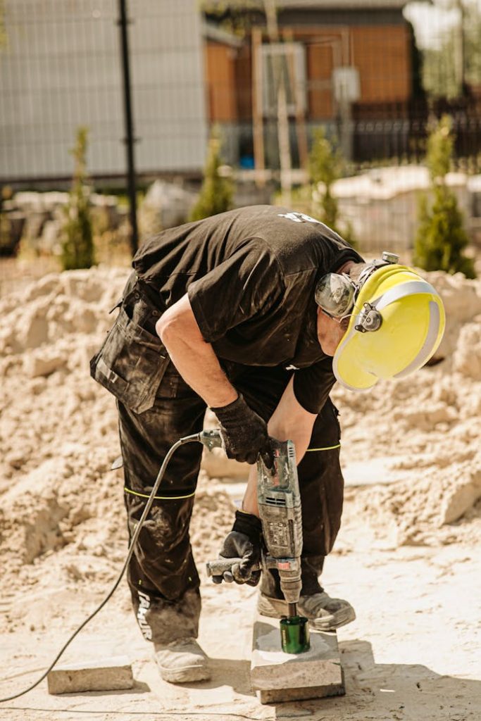 Construction worker using a demolition hammer outdoors during a sunny day.